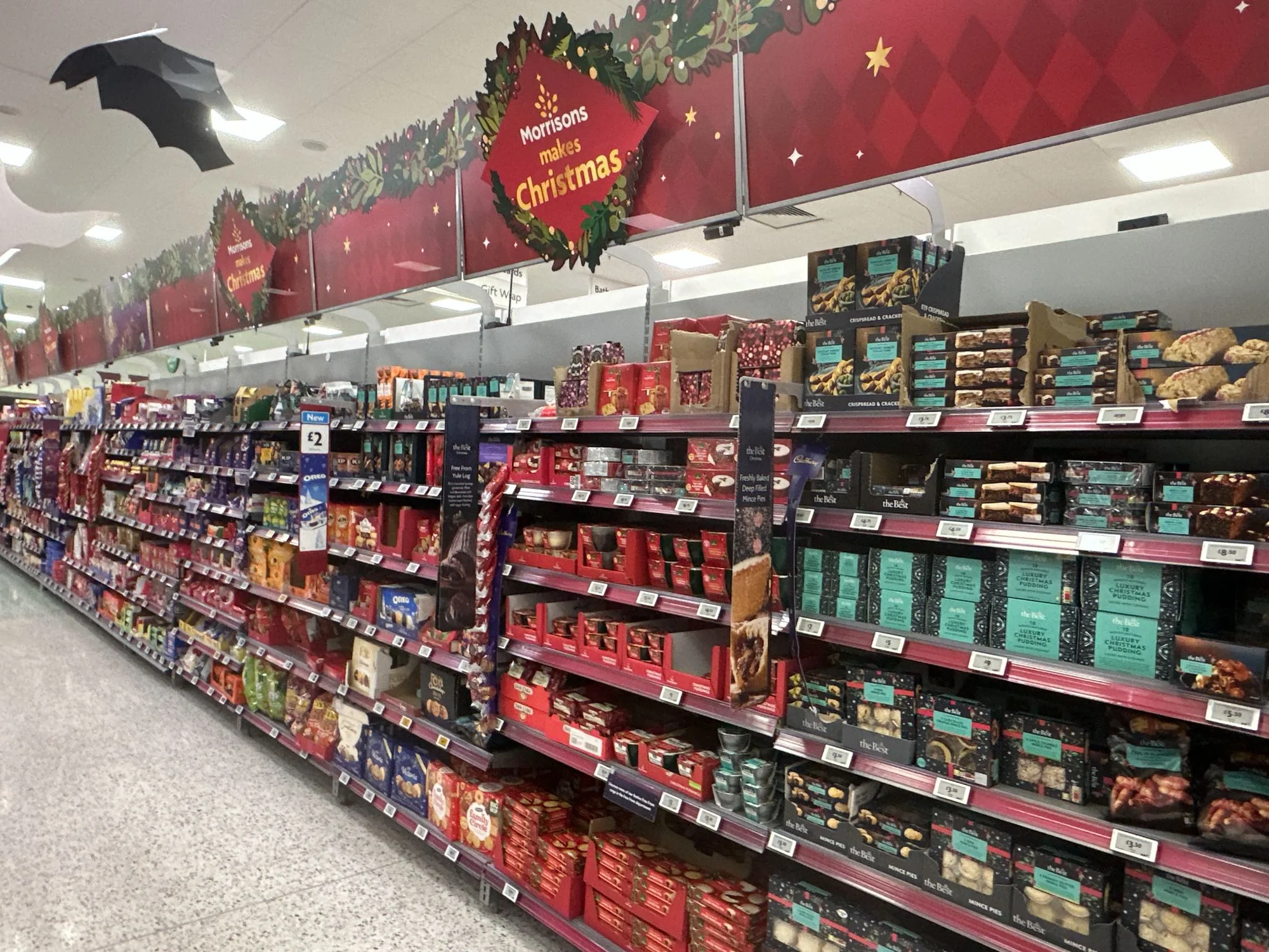 Christmas aisle in a UK supermarket in late October, with a Halloween bat decoration still hanging